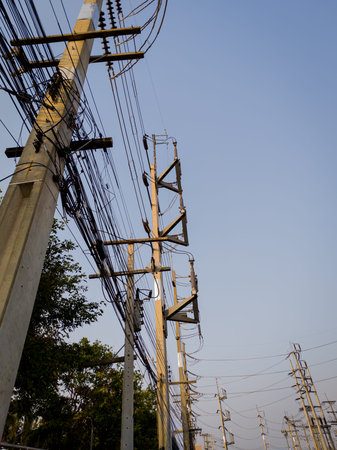Utility poles with high voltage power lines and communication cables under clear sky. Perfect for...