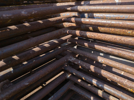 Close-up photo of stacked rusted scaffolding pipes forming geometric patterns. Perfect for...