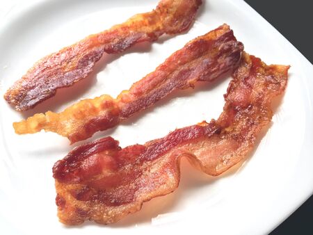 Fried crispy bacon strips on white plateの写真素材