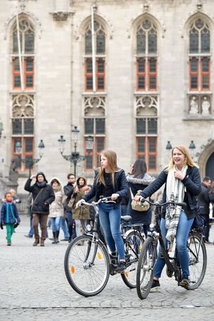 Girls enjoy riding bicycles at Market square, Bruges, Belgiumのeditorial素材