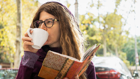Girl with glasses drinking coffee in a white mug looking away from camera wearing a purple hoodie