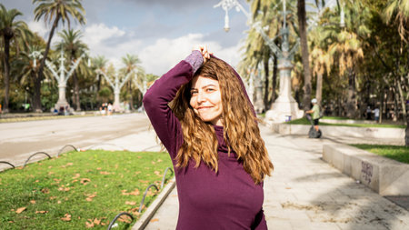 Beautiful girl with a purple hood and glasses and curly hair looking into the camera with both hands placed side and side of the face in a park outdoor environmentの写真素材