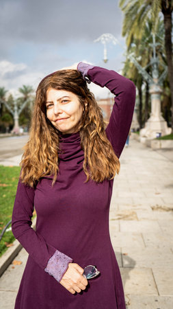Beautiful girl with a purple hood and glasses and curly hair looking into the camera with both hands placed side and side of the face in a park outdoor environmentの写真素材