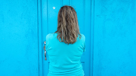 Anonymous woman seen from the back with blonde hair and blue t shirt in a blue backgroundの写真素材