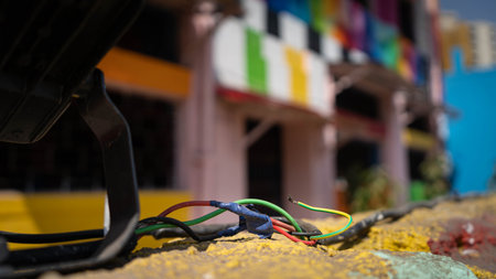 A bunch of colorful wires in the foreground over a yellow wall with a colorful building in the background out of focusの写真素材