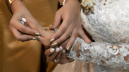 Bride hands while bridesmaid helps her with her bangles in a beautiful momentの写真素材