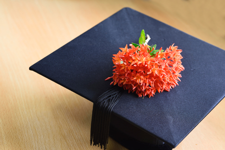 graduates,cap and Red flower spike represents intelligent knowledge on wood backgroundの写真素材