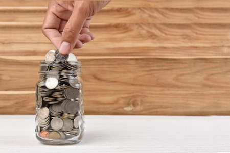 Hand saving coins money into glass on wood background,saving concept.の写真素材
