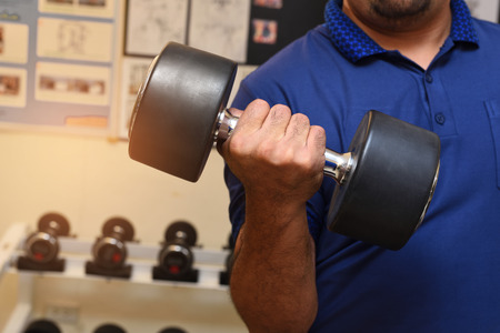 Blue shirt men carry large dumbbell in gym room.の写真素材