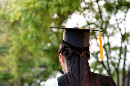 Behind photo of university graduate wears gown and black cap, yellow ribbon and blur bokhe background. の写真素材