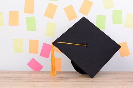 Black graduated cap and yellow tassel on wooden table,Colorful paper note the background