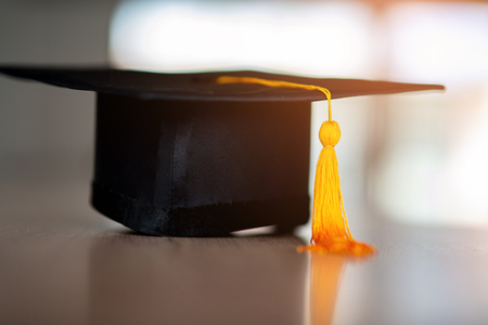 Black hat and yellow tassel of graduates placed on a wooden tableの写真素材