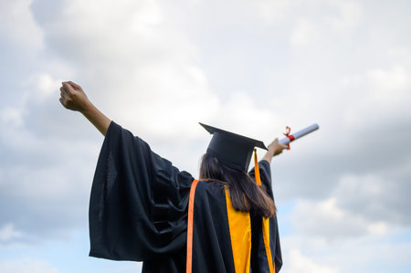 Long haired female students wearing black ruffle dresses expressing joy on graduation at the university.の写真素材