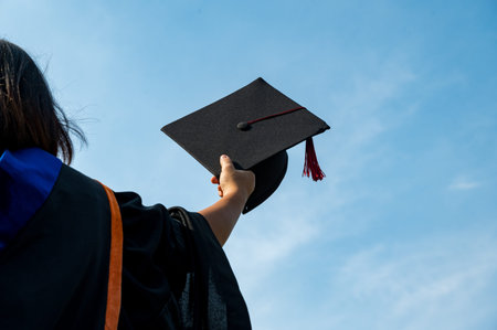 The students holding a shot of graduation cap by their hand in a bright sky during ceremony success...