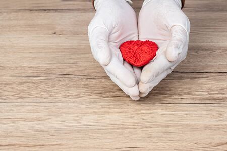 The doctor wrapped his hand around the red heart on the desk,Heart disease concept.の写真素材
