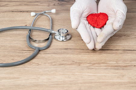 The doctor wrapped his hand around the red heart on the desk,Heart disease concept.