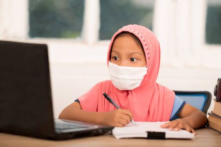 Back to school concept,Muslim girls wearing sanitary masks studying online at home To reduce social distance and prevent communicable diseasesの写真素材