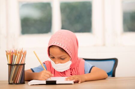 Back to school concept,Muslim girls wearing sanitary masks studying online at home To reduce social distance and prevent communicable diseasesの写真素材