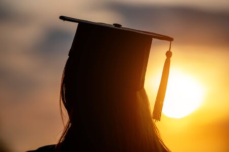 University female graduates Wearing a black robe, wearing a black hat, looking at the sunsetの写真素材