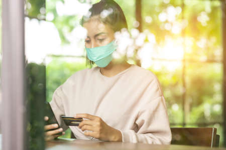 Woman wearing surgical mask in cafe shopping online with Mobile Phoneの写真素材