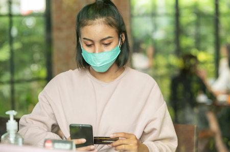 Woman wearing surgical mask in cafe shopping online with Mobile Phone