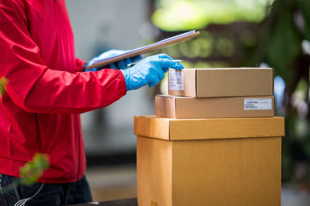 Close up delivery man Wearing blue gloves in red cloth Searching for customer address by mobile phoneの写真素材