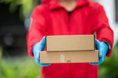 Close up delivery man Wearing blue gloves in red cloth holding a box packageの写真素材