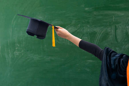 Close up hand of Graduate holding Graduation hat on the green chalkboard background,Education Success Conceptの写真素材