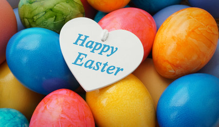 Happy Easter greeting message on a white wooden heart and eggs painted in many different colors on...
