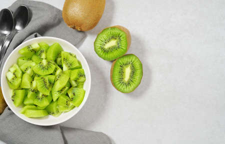 Kiwifruit fresh summer salad with sliced green kiwi in a white bowl on a light gray table top view with copy space.の写真素材