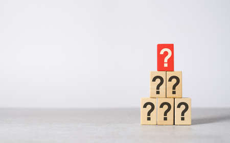 Main question concept with a question mark printed on a red wooden block on top of others black questions with copy space on light grey background.の写真素材