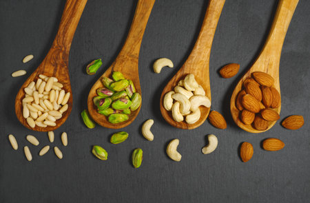 Nuts mix with pine nuts, pistachios, cashews nuts and almonds in wooden spoons top view closeup on...