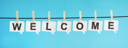 Welcome word and sign on white paper speech bubbles hanged on blue background for welcoming concept.の写真素材