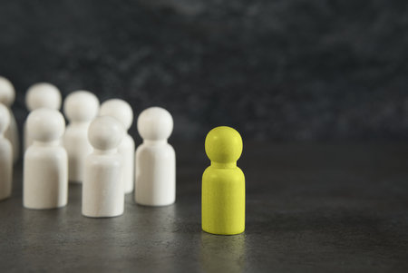 Stand out, new ideas and leadership in business concept with a yellow wooden pawn leader standing out and leading among the others on dark gray background.の写真素材