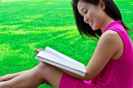 Young women reading a book in the green grass の写真素材