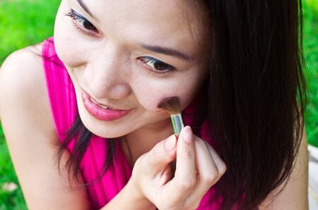 Asian young woman applying make up outdoorsの写真素材