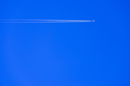 Flying airplane on the blue sky leaving white lines behindの写真素材