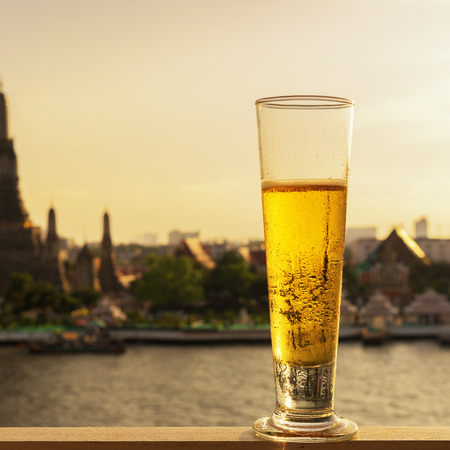 Tall glass of beer  with The view of Wat Arun, Landmark in Bangkok.の写真素材