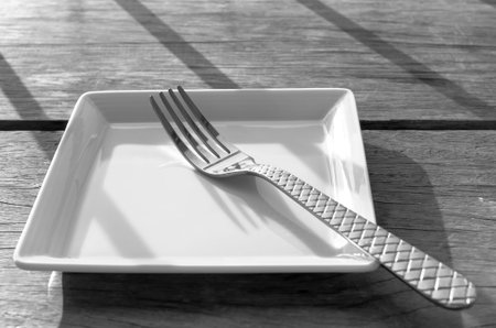 Empty plate and fork on wooden table with a light splash. Sunset
