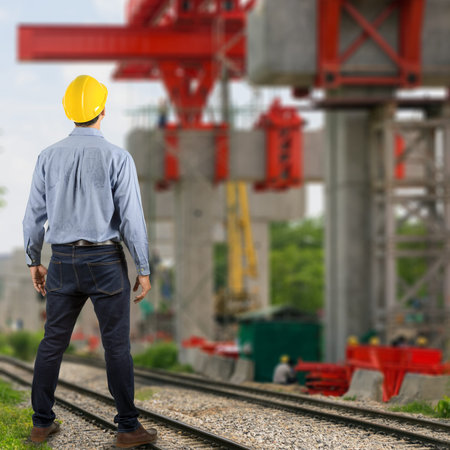 Asian engineers monitor the construction project with large red crane in the background.