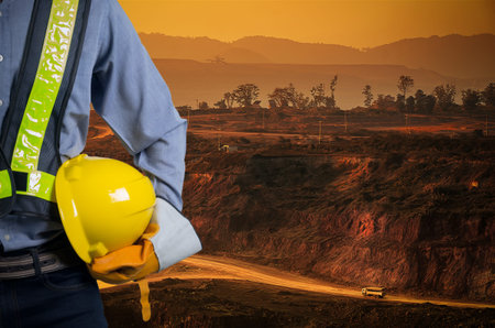 Engineer holding a yellow helmet for the safety of workers on a background of coal mining trucks are...