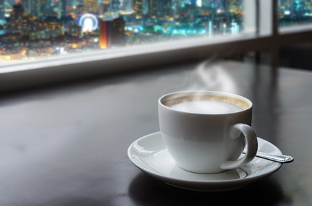 Warm white coffee cup on the table. With the backdrop of a beautiful city at night.の写真素材