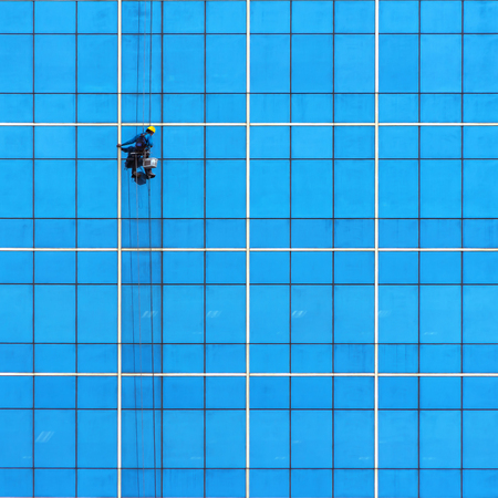 Cleaning staff windows on tall buildings. Wearing yellow helmet hanging by a rope sling, high risk workの写真素材