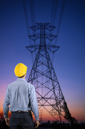 Engineer holding a yellow helmet for the safety of workers on the background. Silhouette transmission towers on the background of the evening sun.の写真素材
