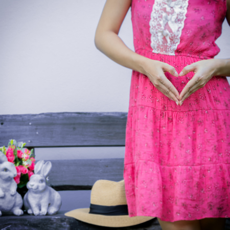 Pregnant woman holding her hands in a heart shape on the pink dress.の写真素材