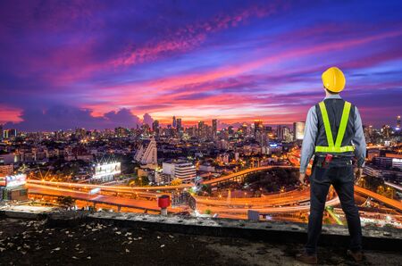 Engineer holding a yellow helmet for safety of the workers. A modern high-rise structures in the background.の写真素材