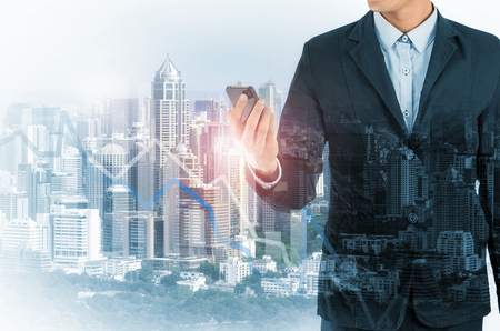 Double Exposure of a businessman using a smartphone and cityscape in the background, with Forex graph data.の写真素材
