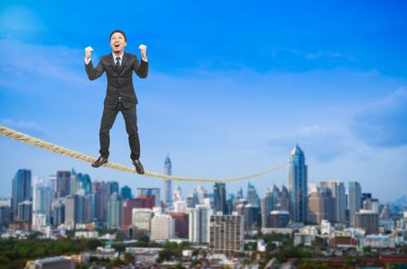 Businessman standing on a rope over blurred cityscape.の写真素材