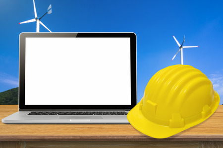 Yellow safety helmet and laptop on desk with industry background, blank on screen.の写真素材