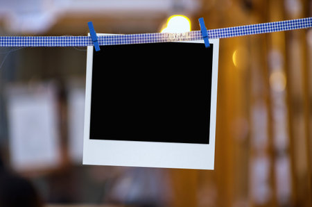 Blank photo frame with clothespin hanging on blurred light background.
